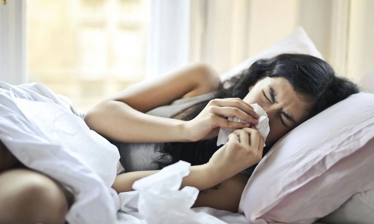 Mujer recostada sobre una almohada sosteniendo un pañuelo sobre su nariz.