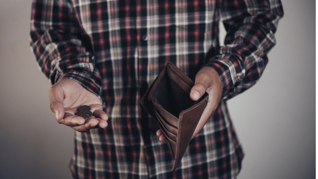 hombre con una cartera vacía y algunas monedas en la mano 