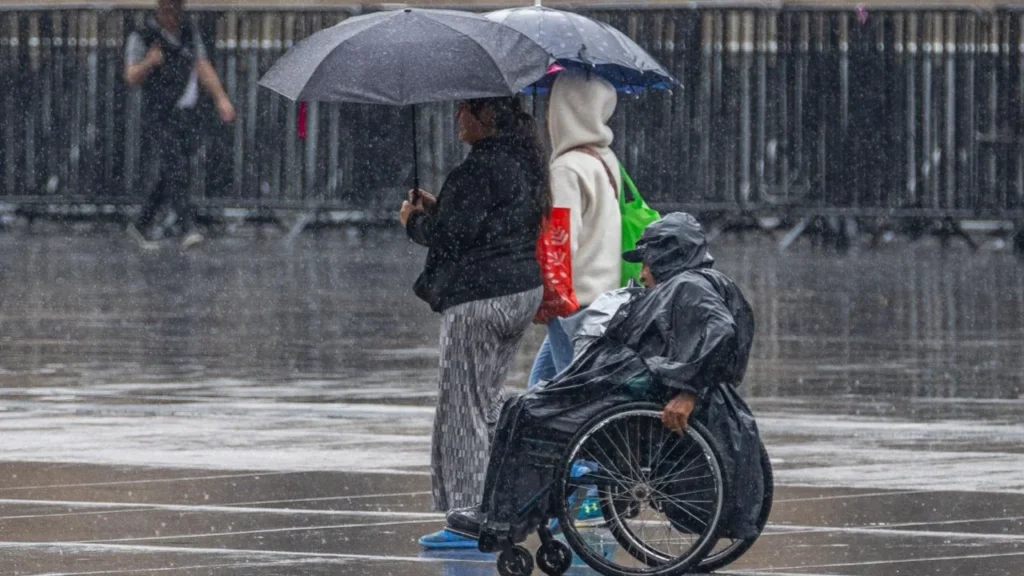 Personas cubriéndose con paraguas o impermeables tras llovizna ligera en el Zócalo de la Ciudad de México.