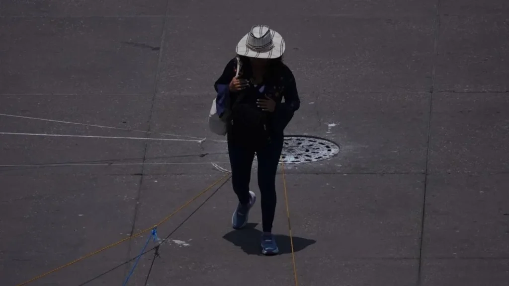Una joven se protege de los rayos del sol con sombrero y ropa de manga larga debido al clima caluroso en la capital 