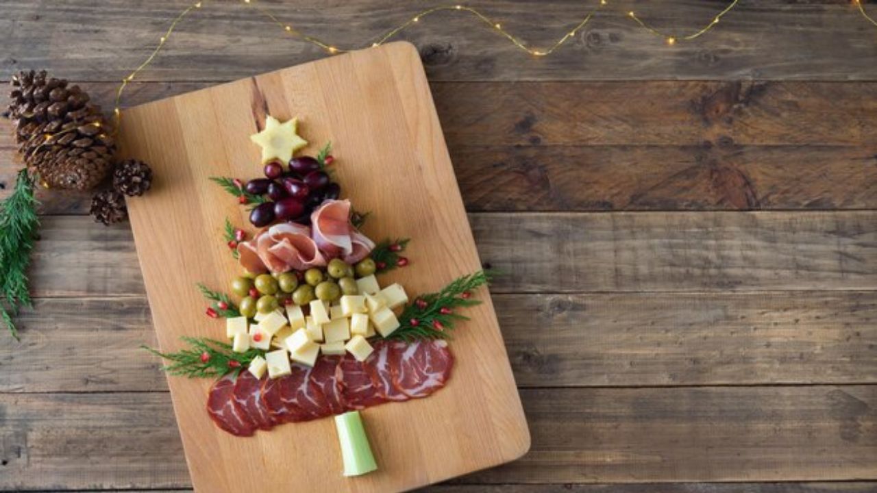 Tabla de carnes frías, conservas y quesos montada en forma de árbol de navidad, sobre una tabla de madera. 