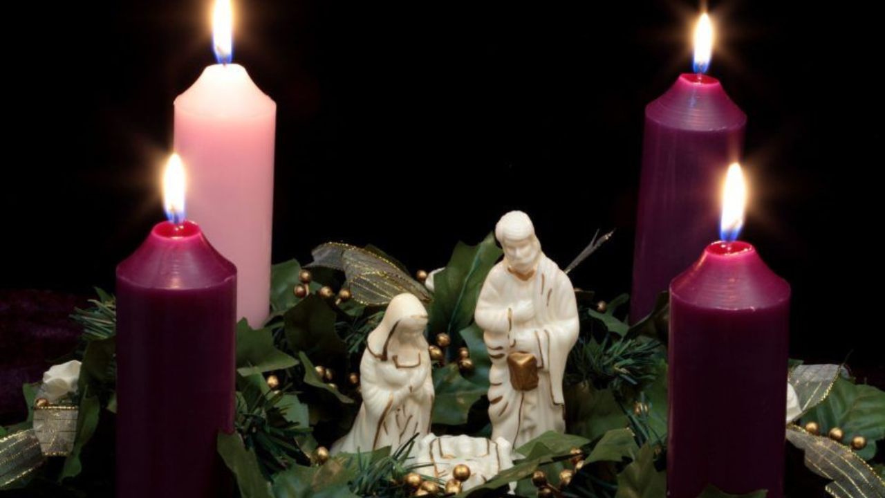 Corona de adviento con tres velas moradas y una rosa, encendidas.