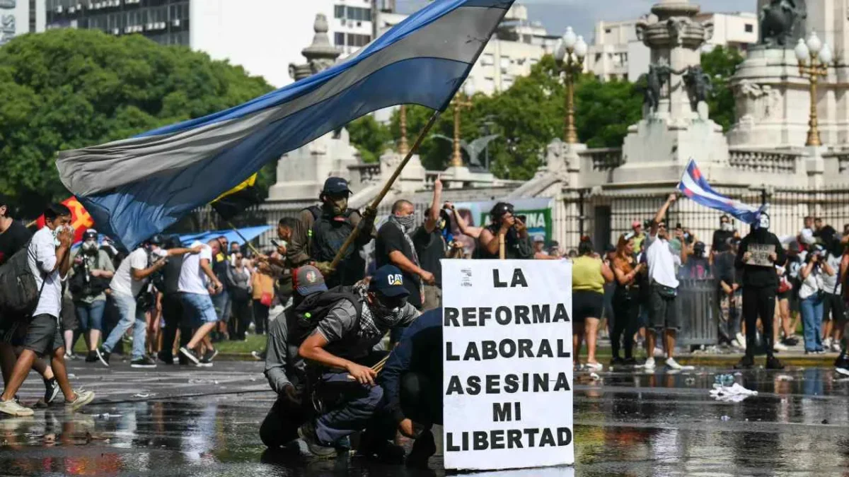 MALESTAR. Manifestantes se cubren con una manta del chorro de agua lanzado por la policía durante la protesta contra la reforma laboral, en Buenos Aires.