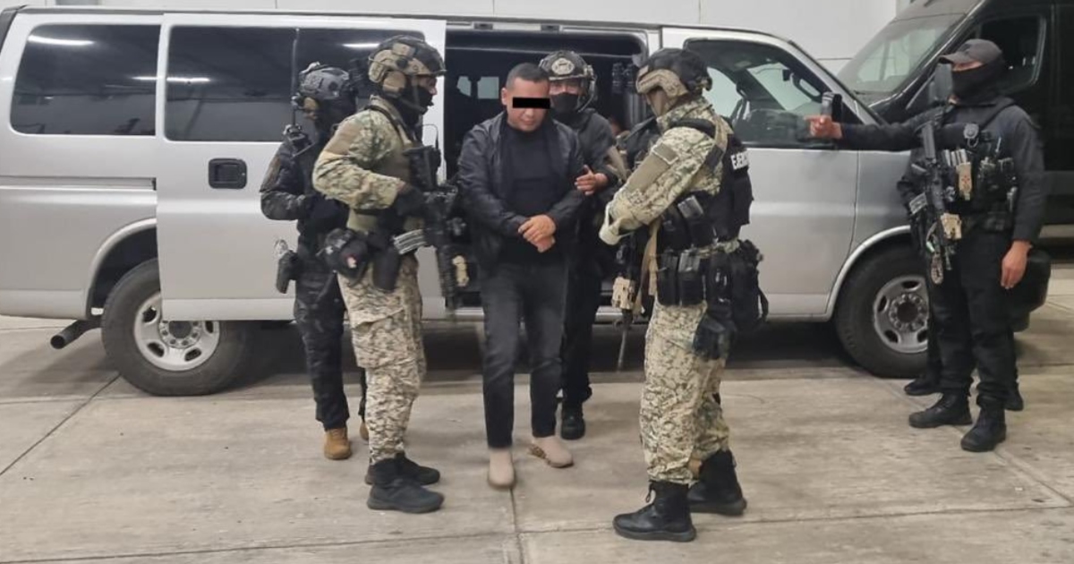 momento en que un sujeto detenido, identificado con el alias de «El Tanque» (presunto operador del CJNG en Jalisco), es traslada y escoltado por fuerzas de seguridad federales. El individuo viste chamarra negra, pantalón gris y lleva el rostro censurado mediante una franja negra. Es sujetado de los brazos mientras camina frente a una camioneta van de transporte táctico de color gris con la puerta corrediza abierta, rodeado por elementos del Ejército y fuerzas especiales con uniformes camuflados, chalecos antibalas, cascos y rostros cubiertos con pasamontañas.