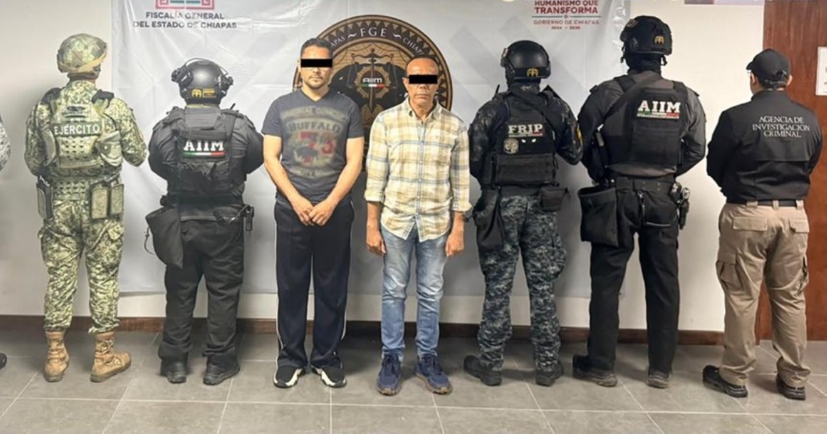 Fotografía oficial de presentación en plano general que muestra a dos hombres detenidos con el rostro censurado con una franja negra. Ambos se encuentran de pie en el centro, custodiados por seis elementos de seguridad fuertemente armados pertenecientes al Ejército Mexicano, la Fuerza de Reacción e Intervención Policial (FRIP), la Agencia de Investigación e Intervención Marítima (AIIM) y la Agencia de Investigación Criminal (AIC). Al fondo se observa una lona institucional de la Fiscalía General del Estado de Chiapas con los logotipos oficiales de la dependencia y del gobierno estatal.