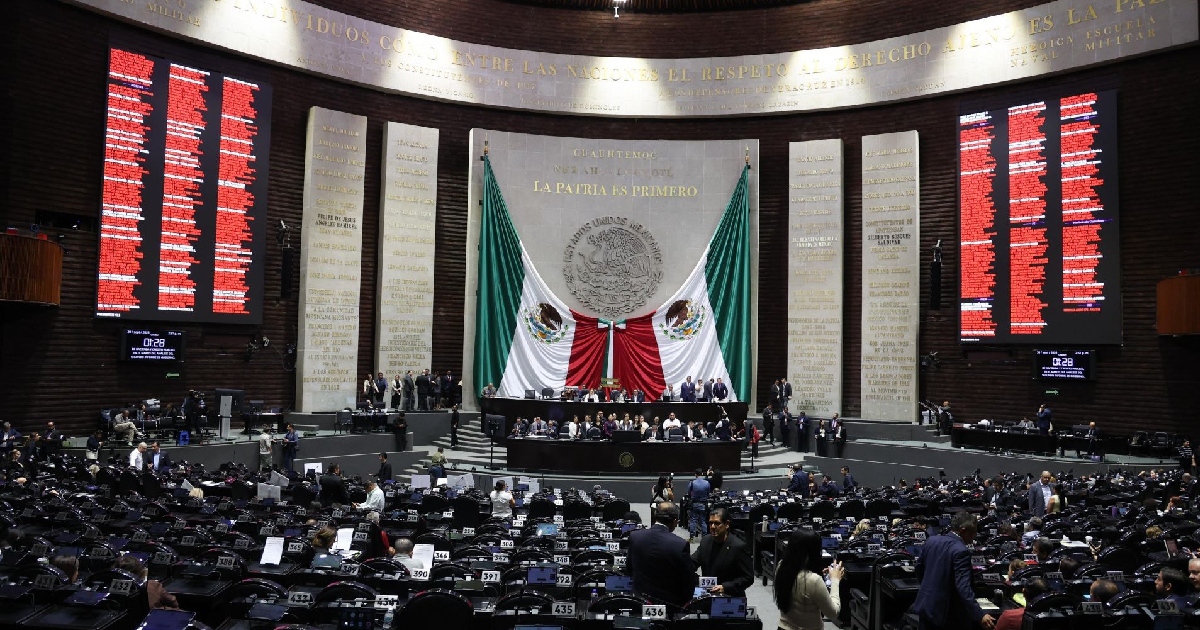 pleno del Palacio Legislativo de San Lázaro en la Cámara de Diputados de México. Al fondo destaca el Muro de Honor con la leyenda en letras doradas «LA PATRIA ES PRIMERO» y la Bandera Nacional monumental flanqueada por las placas conmemorativas. A los lados se observan los grandes tableros electrónicos con la votación reflejada en color rojo, mientras los diputados ocupan sus curules durante el debate y votación del dictamen.