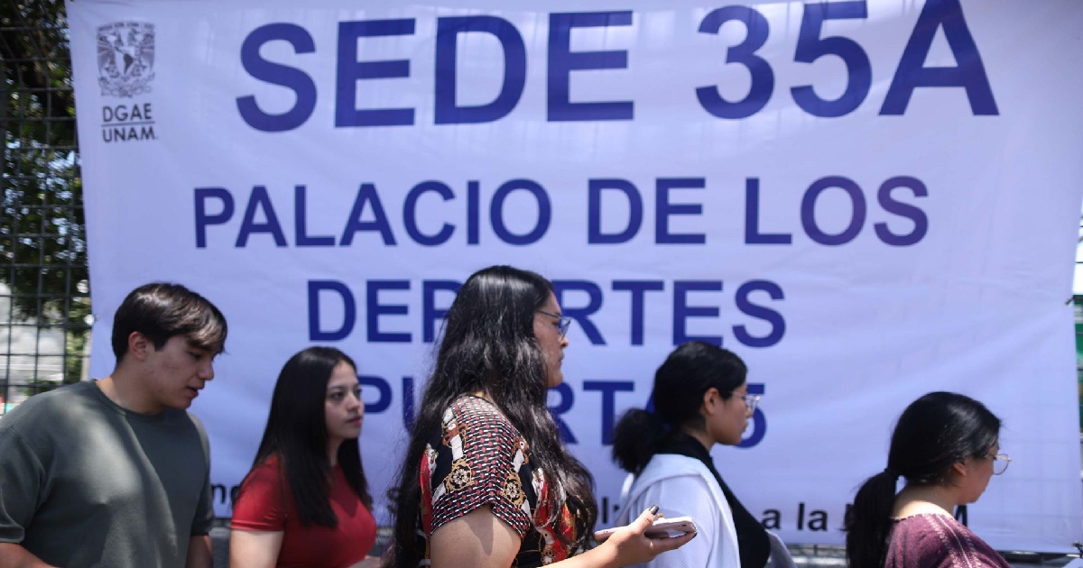 Aspirantes caminan frente a una gran manta blanca oficial de la Dirección General de Administración Escolar (DGAE UNAM) colocada en el Palacio de los Deportes. La lona muestra letras grandes de color azul marino con el texto «SEDE 35A PALACIO DE LOS DEPORTES PUERTA 5» junto al escudo de la DGAE UNAM.