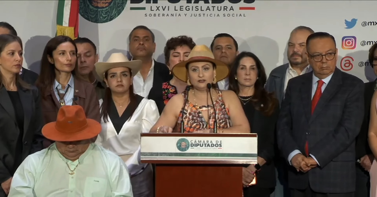 Plano medio durante una rueda de prensa en el pódium institucional de la Cámara de Diputados (LXVI Legislatura). Al centro, la diputada Guadalupe Araceli Mendoza Arias emite un mensaje luciendo un sombrero de ala ancha color verde oliva/marrón y una prenda con estampado tradicional.