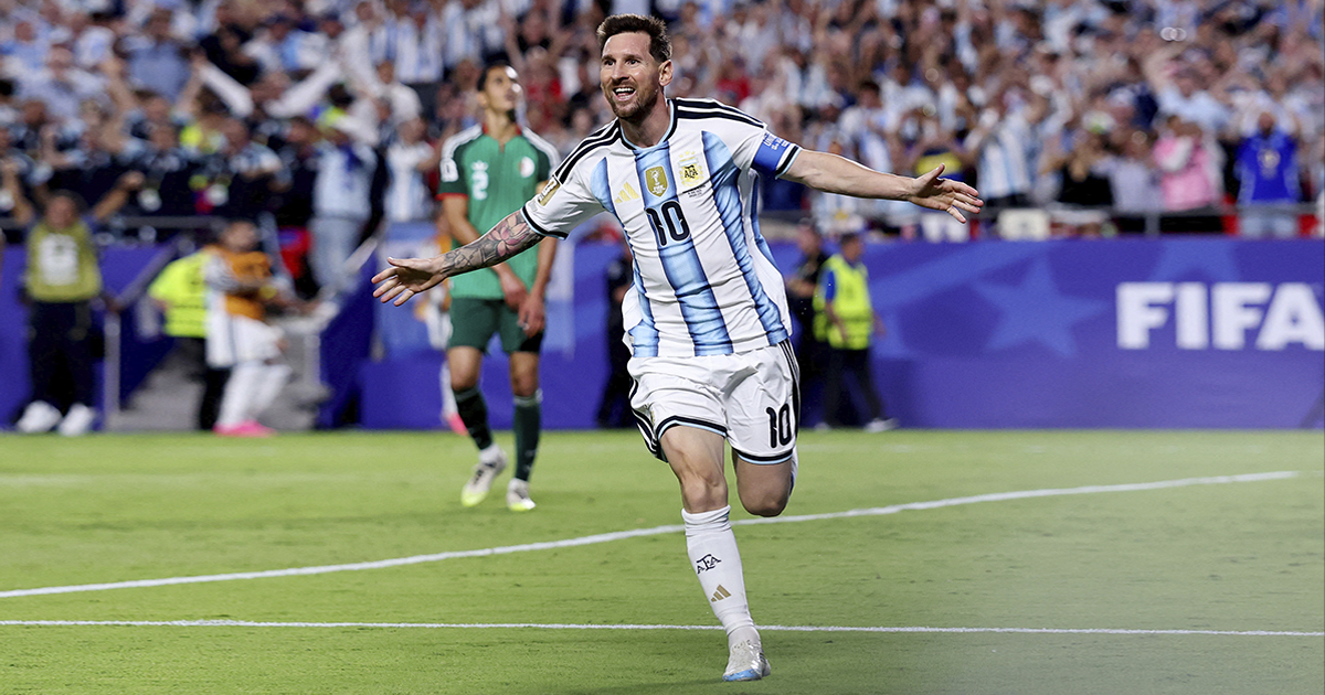 Lionel Messi corriendo con los brazos abiertos en plena celebración de un gol con la camiseta número 10 de la Selección Argentina. Porta la cinta de capitán en el brazo izquierdo y luce el parche de campeón del mundo en el pecho.