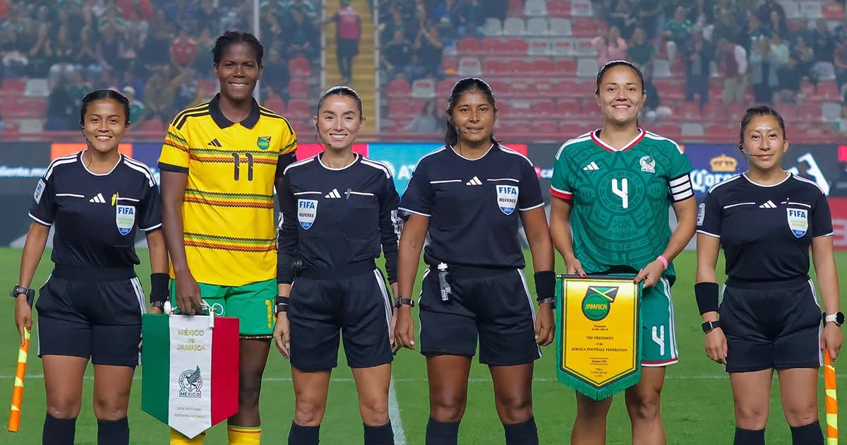 protocolo previo al partido entre las selecciones femeniles de México y Jamaica en el Estadio Victoria de Aguascalientes. Al centro se ubican la capitana de Jamaica (Khadija Shaw, con la camiseta amarilla número 11) sosteniendo el gallardete con la bandera de México, y la capitana de la Selección Mexicana Femenil (Rebeca Bernal, con el jersey verde número 4) sosteniendo el gallardete oficial de la Federación de Fútbol de Jamaica. Junto a ellas posa el cuarteto arbitral de la FIFA, vistiendo uniformes oficiales negros con parches e insignias del arbitraje internacional.