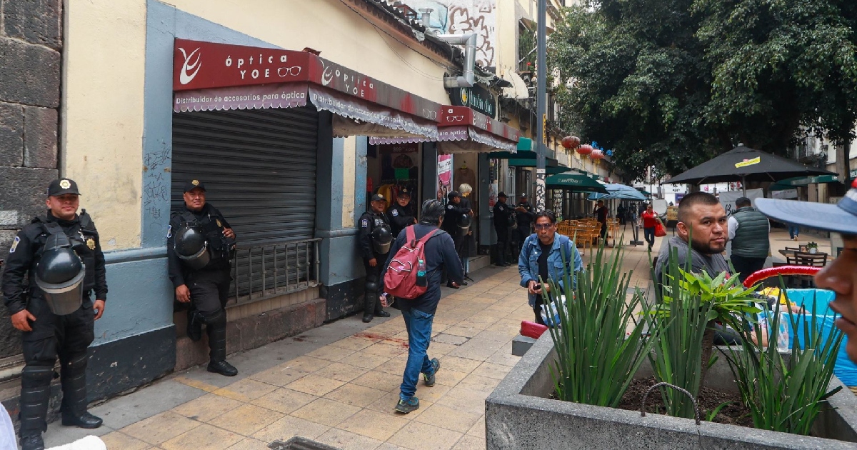 Policías antimotines resguardando establecimientos; en el suelo, una mancha de sangre