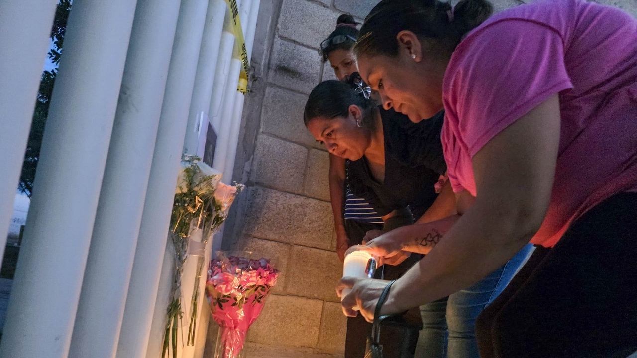 Una mujer coloca una veladora al exterior de una reja 