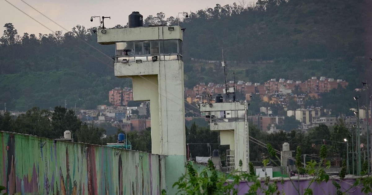 perímetro de un reclusorio varonil en la Ciudad de México. En primer plano destaca el bardo o muro de contención perimetral pintado con murales en tonalidades verdes. Por encima del muro se erigen dos torres de vigilancia metálicas y de concreto de varios niveles, equipadas con sistemas de videovigilancia y cámaras de seguridad.