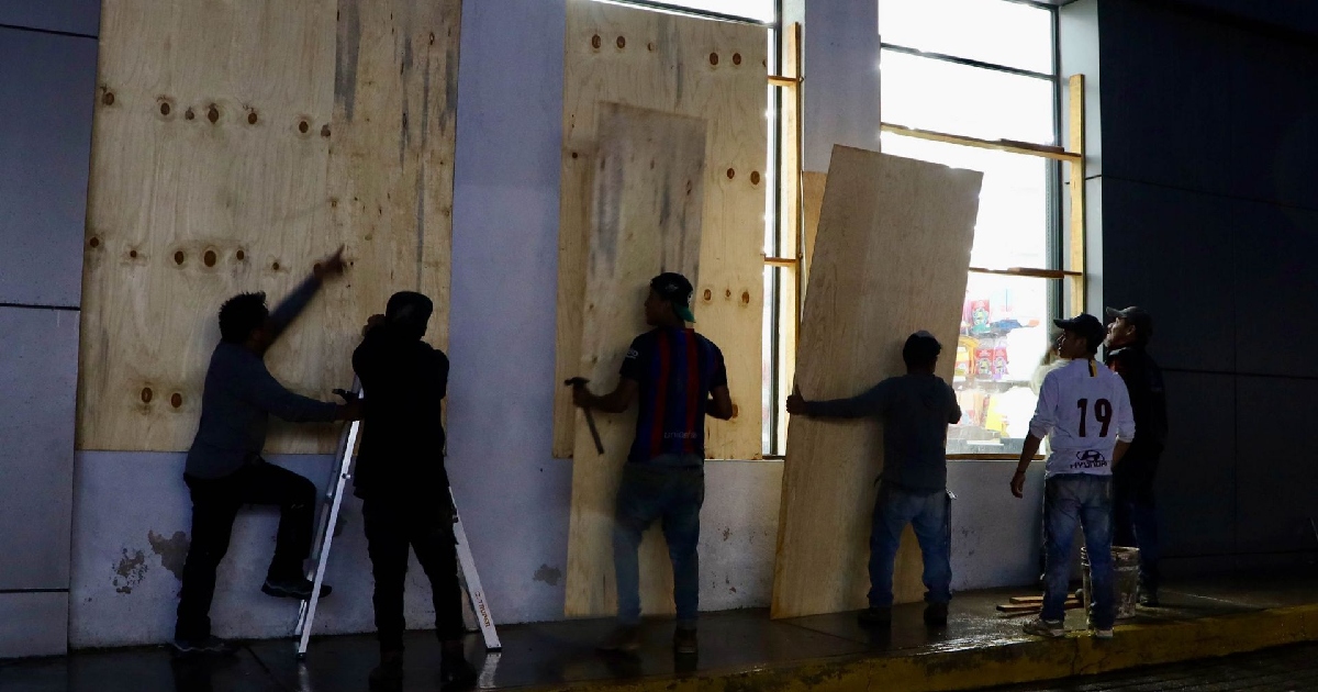 Un grupo de personas colocan tablas de madera sobre las ventanas de un edificio para resguardarse ante la llegada de un huracán 