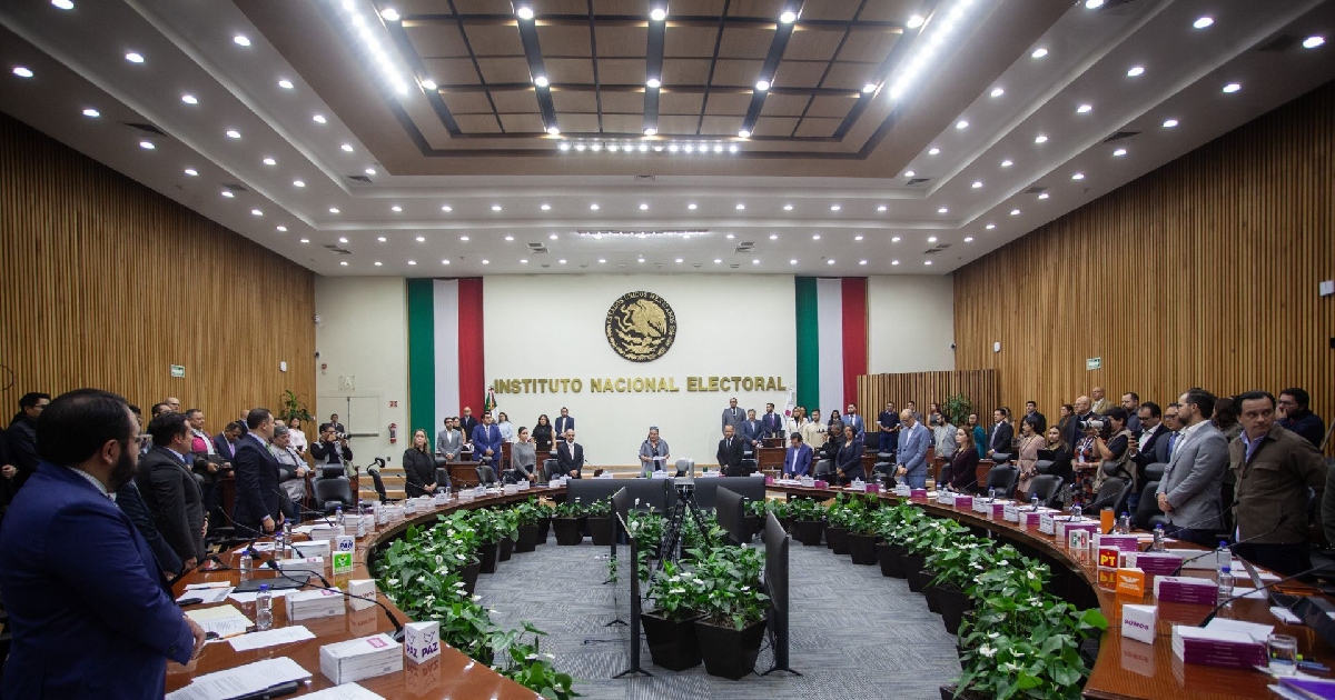 lano general del Salón de Sindicatos / Consejo General del Instituto Nacional Electoral (INE). Se observa la mesa semicircular de herradura con los lugares de las consejeras y consejeros electorales, representantes de partidos políticos e invitados de pie durante el desarrollo de una sesión extraordinaria. En el muro testero destaca el Escudo Nacional de México flanqueado por lienzos con los colores patrios y las letras doradas con la leyenda «INSTITUTO NACIONAL ELECTORAL».