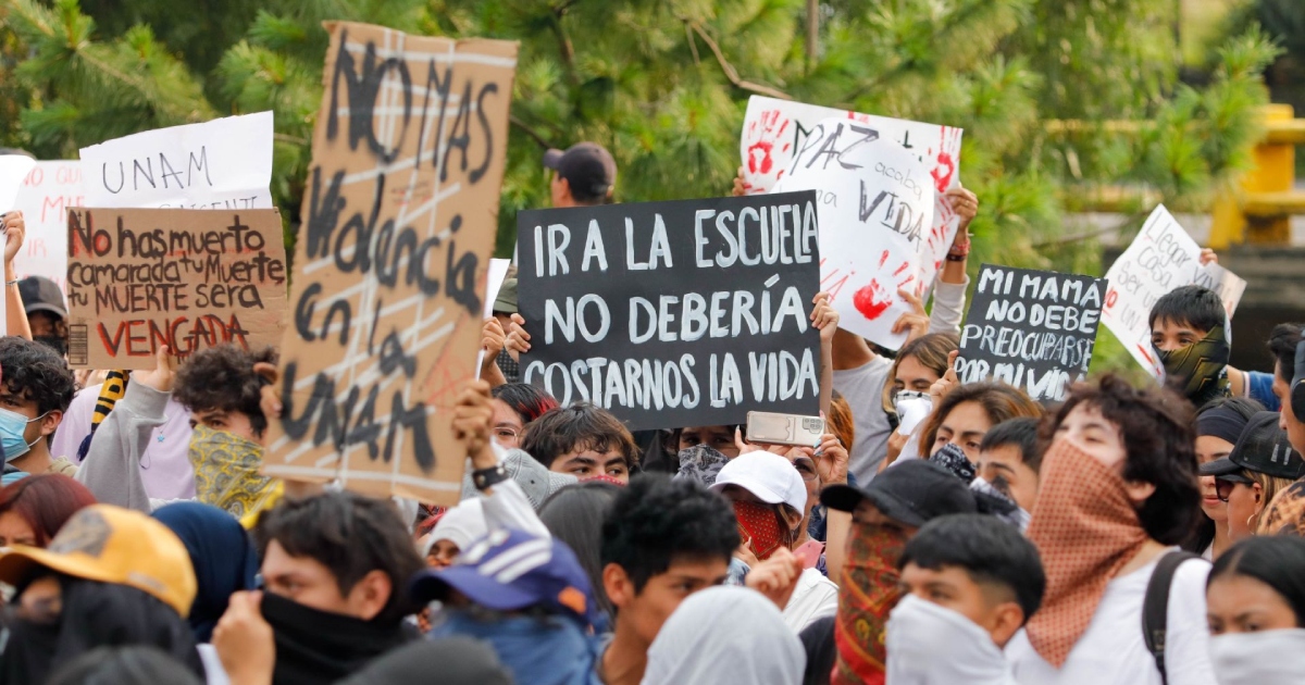 anifestación estudiantil masiva en la vía pública. En la marcha, jóvenes y estudiantes sostienen diversos carteles de protesta elaborados en cartón y cartulina con mensajes centrados en la seguridad universitaria, tales como «Ir a la escuela no debería costarnos la vida» y «No más violencia en la UNAM»
