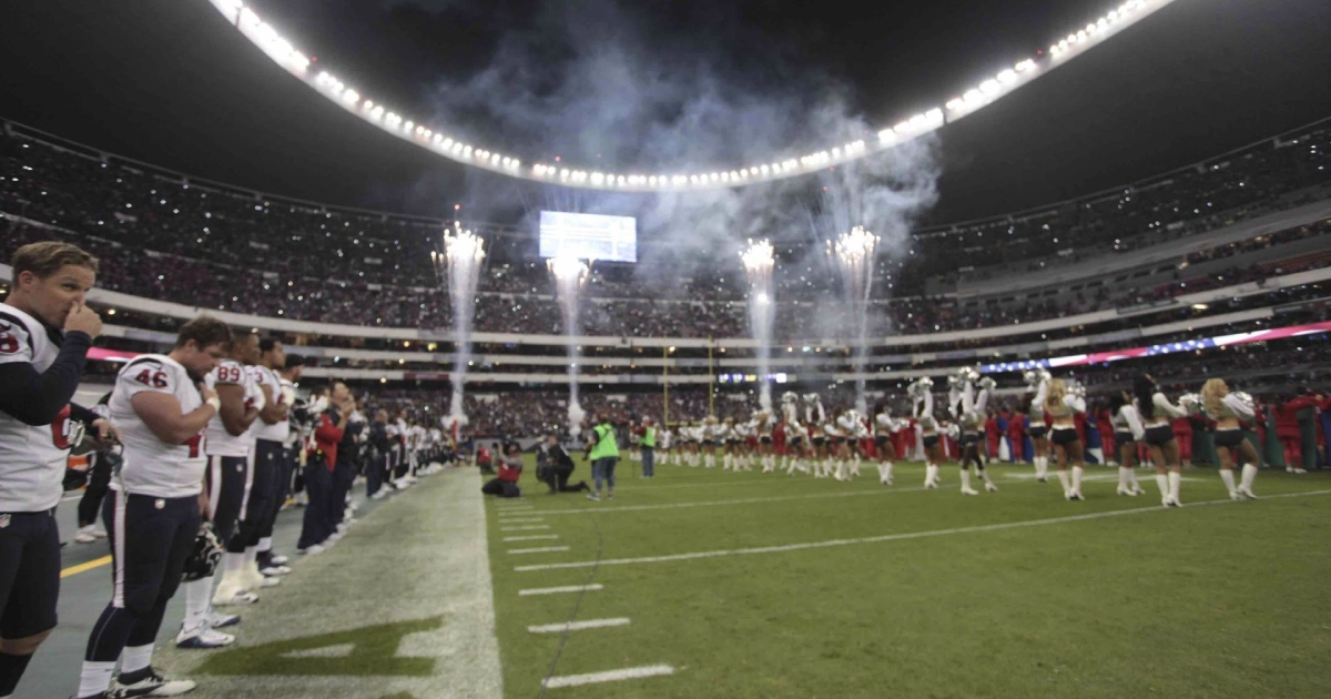 Vista a nivel de cancha en el Estadio Azteca durante el protocolo de apertura de un partido de la NFL en Ciudad de México. En el costado izquierdo se observa en fila a los jugadores de los Houston Texans