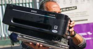 n ciudadano cargando dos aparatos electrónicos obsoletos hacia un centro de acopio durante la jornada del Reciclatrón en la Ciudad de México. El ciudadano lleva en las manos una impresora de inyección de tinta marca Epson sobre un reproductor de DVD marca Samsung.